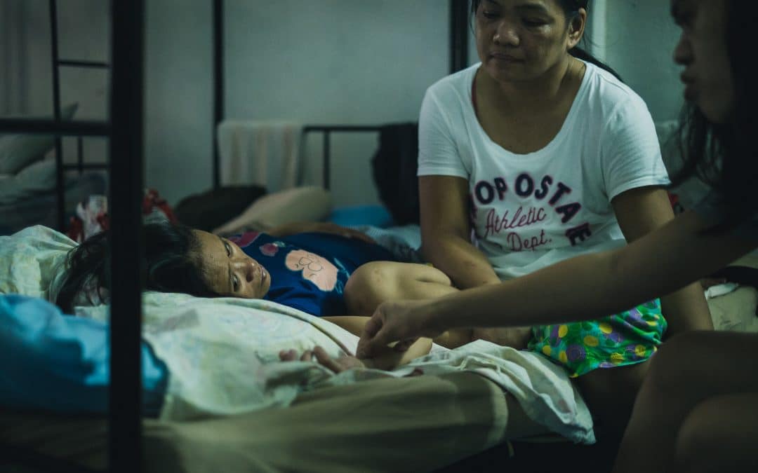 A woman tenderly assisting another women lying in a bed, providing care and support to ensure their well-being.