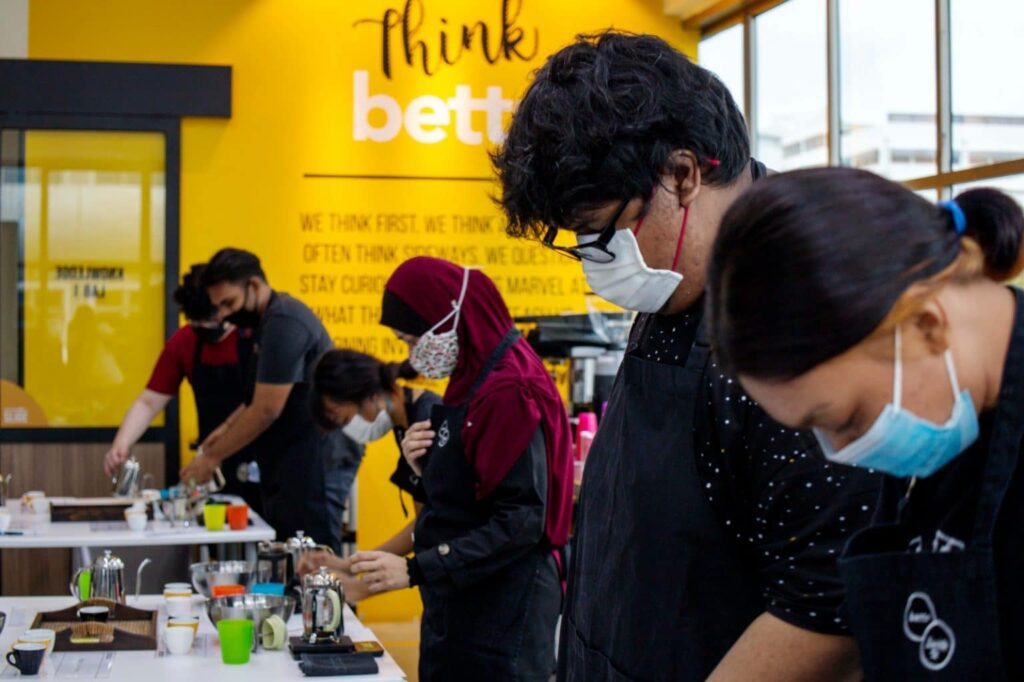 People in masks and aprons preparing food in a restaurant.