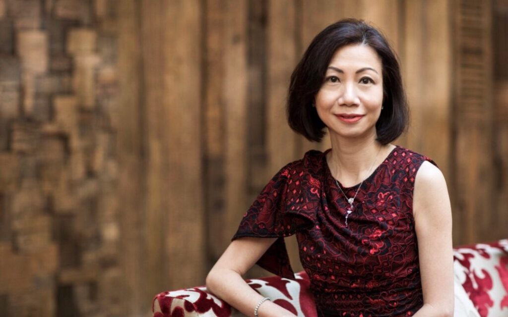 An Asian woman (Catherine) gracefully seated on a vibrant red and black couch, exuding elegance and poise.