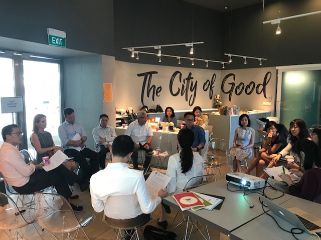 A diverse group of individuals gathered around tables in a well-lit room, engaged in conversation and collaboration.