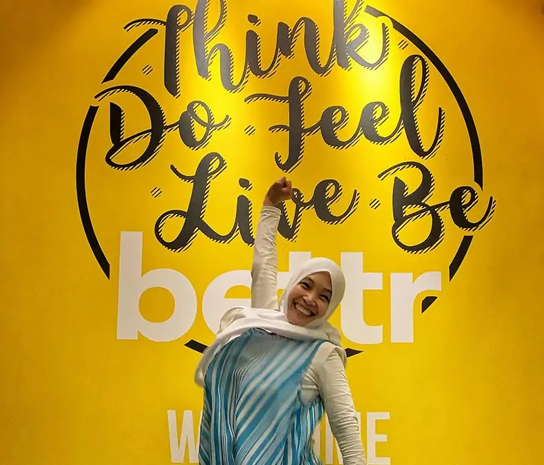 Lady in blue dress standing in front of vibrant yellow backdrop.