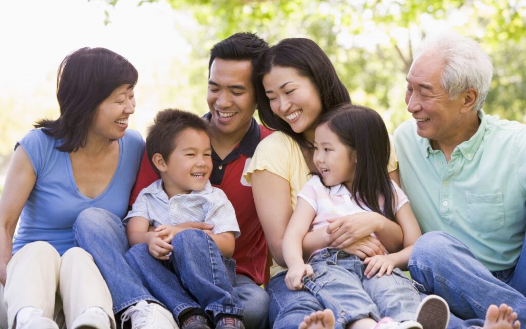 An Asian family enjoying quality time together, sitting on the lush green grass in a serene park setting.